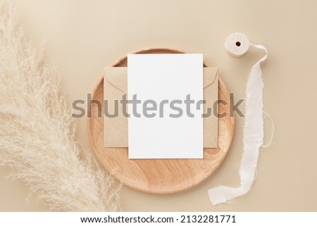 Blank greeting card invitation Mockup on Brown envelope with pampas grass on beige background, Minimal table workplace composition, flat lay, mockup