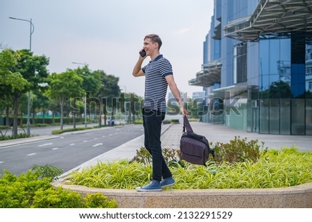 Young caucasian man in casual clothing with the backpack walking near modern office buildings and making phone call. people using phone. High quality