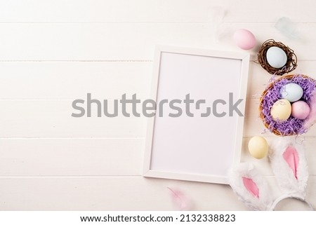 Easter holiday mockup. White frame with easter decorations eggs, feathers and bunny ears flat lay on beige background