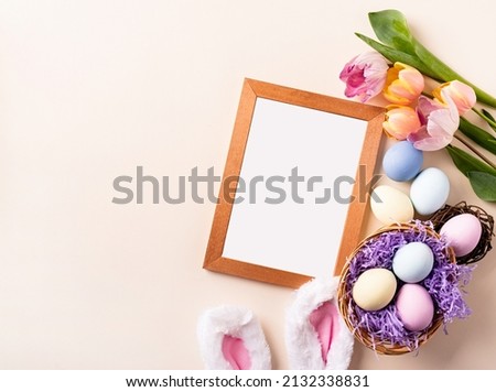 Easter holiday mockup. Wooden frame with easter decorations eggs, tulips and bunny ears flat lay on beige background