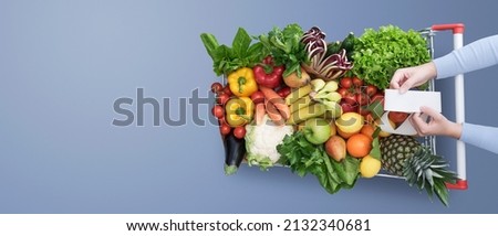 Woman buying a lot of fresh vegetables and fruits, she is checking the grocery receipt, top view