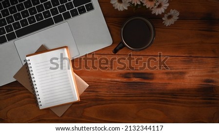 Laptop computer, notebooks, coffee cup and flower pot on wooden background. Top view.