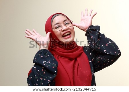 An Asian Muslim lady raising both of her hands to her face and laughing. Happy and playful expression.