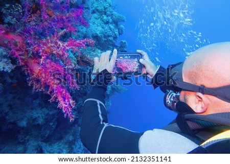 Man scuba diver using smartphone underwater housing when shooting coral reef scenery. Modern smartphone technology.