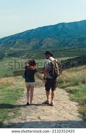 A couple of tourists in hats, a man with a backpack. walk against the backdrop of the mountains. Mtskheta. Georgia. Vertical photo