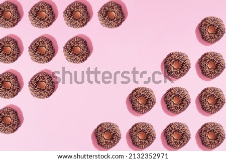 Arranged ring donuts like triangle with chocolate glaze and small crumbs on a pink pastel background. Minimal design and copy space.