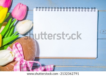 Easter holiday greeting card background, with chocolate easter bunny, eggs, and tulip flowers, on light blue background flatlay frame copy space top view