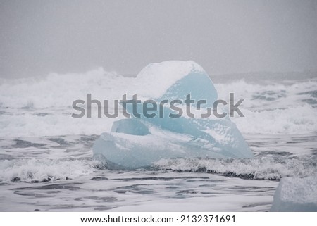 Blue iceberg on the black sand beach with vases in the background. Captured in winter in Iceland at the Diamond beach.
