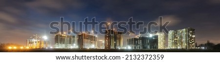 View of a large construction site with buildings under construction and multi-storey residential homes.Tower cranes in action on night sky background. Panoramic view.