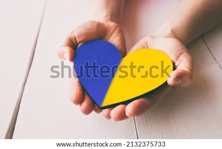 The wooden heart in colors of Ukrainian flag in woman's hands