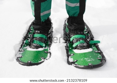 man walks in green snowshoes. winter hike on the white snow road