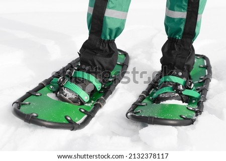 man walks in green snowshoes. winter hike on the white snow road