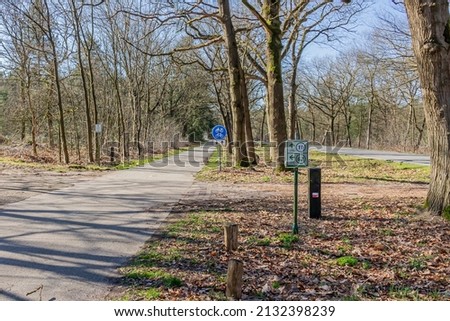 Cycle lane in both directions next to a country road, sign indicating: bike and moped path, routes 11 and 62, bare trees, trails, sunny day with a clear blue sky in the Netherlands