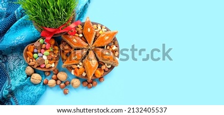 Nowruz festive table. Green wheat grass with red ribbon, arabic dessert baklava, sweets, nuts, dry fruits on blue background. Spring equinox in March, Nowruz Holiday. top view. banner