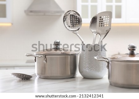 Stainless steel pots and kitchen utensils on white table indoors Royalty-Free Stock Photo #2132412341