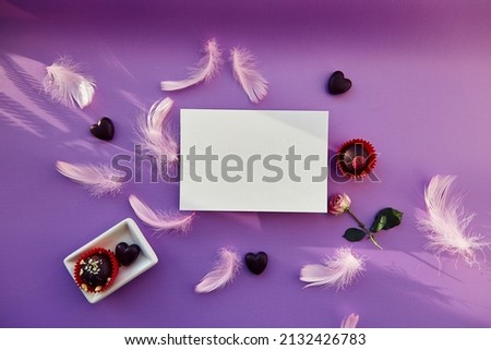 White mock up on purple background with chocolate sweets and pink feathers. Trendy shadows. Holiday present concept. Purple pattern, copy space.