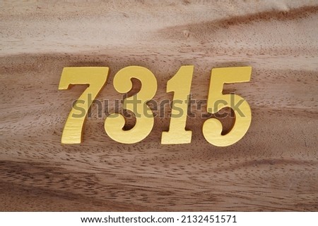 Wooden  numerals 7315 painted in gold on a dark brown and white patterned plank background.
