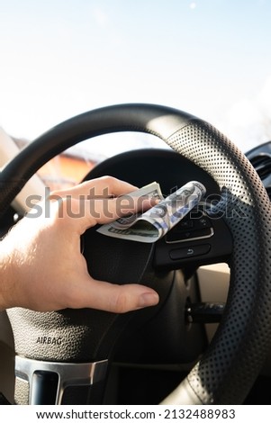 hands of a young man holding new dollar bills on a background of new cars. Car buying and selling concept
