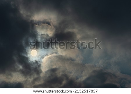 Photograph of full Moon between heavy clouds. Dark cloudy gloomy sky.