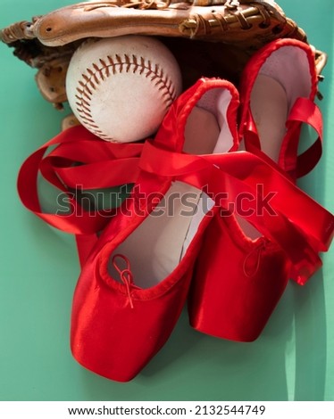 Bright red ballet pointe shoes, grouped with softball and mitt.  Against a teal or green background. 