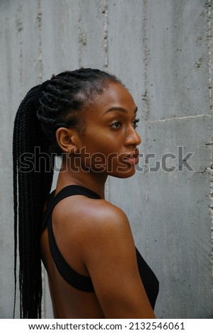 Vertical side portrait of young woman with braids posing on grey background.