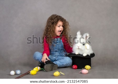Little girl with a rabbit in a hat plays on the Easter holidays. Gray background for copying
