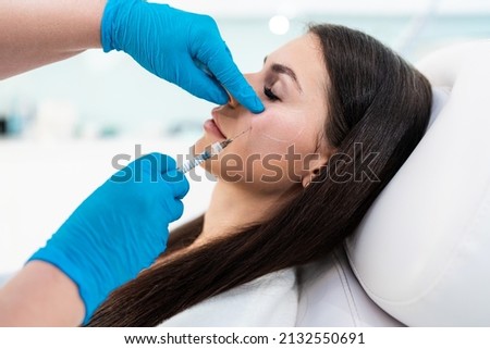 Beautician is contouring the woman's cheekbones with hyaluronic acid filler. Hyaluronic acid filler is injected by needle or cannula. Face contouring concept. Royalty-Free Stock Photo #2132550691