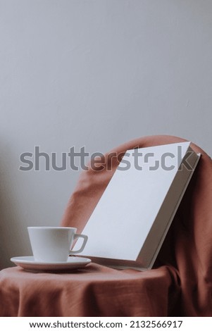 White book and plain cup on pink cloth on gray background for mockup