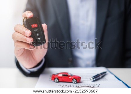 Businessman hand holding remote keyless with car toy, pen and contract document. buy and sale, insurance, rental and contract agreement concepts