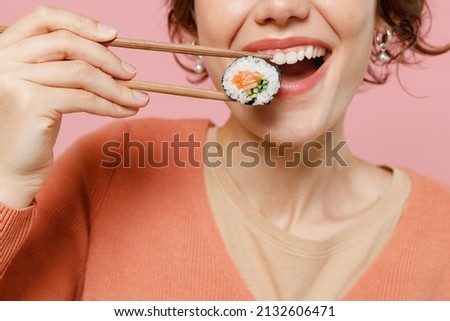 Cropped young smiling happy cheerful fun satisfied cool woman 20s in casual clothes hold in hand makizushi sushi roll traditional japanese food look camera isolated on plain pastel pink background.