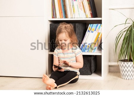 Little child sits on the floor in his room and uses the phone. Childhood communication, technology and communication concept