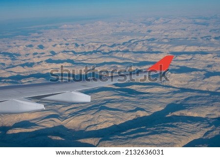 View of the hills of snow-capped mountains from the window of the airliner