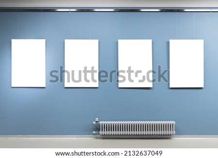 Four blank white vertical posters hang on blue wall in an exhibition hall. Empty interior, front view, background photo