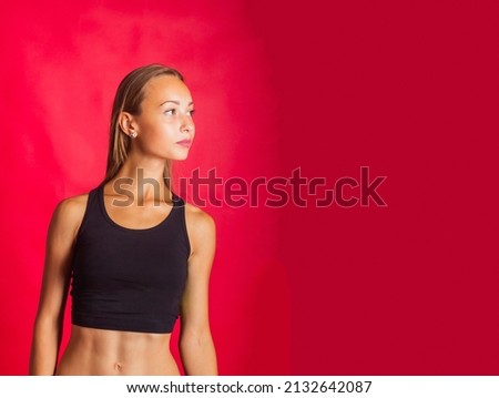 Cheerful active woman is engaged in fitness. Positively fit lady in sportswear is sitting on her knees. Sports activities. Photo taken in studio on isolated red background 