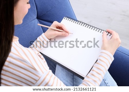 Young woman drawing in sketchbook indoors, closeup