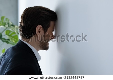Unhappy hysterical young businessman employee manager hitting head against wall, feeling stressed having difficult tasks or problems on work, professional burnout, depression, overworking concept. Royalty-Free Stock Photo #2132665787