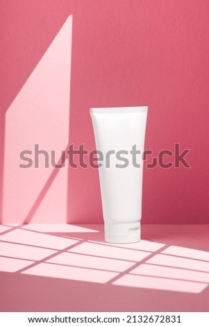 Plastic white tube for cream or lotion. Skincare or sunscreen cosmetic in top view on pink background with shadow. Beauty concept for face care
