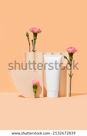 White plastic tube with face, hand and body cream on an orange background with flowers and geometric forms