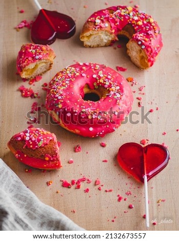 donuts with pink icing and two heart-shaped lollipops close-up on a wooden table