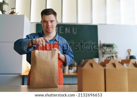 Cheerful young Down Syndrome waiter working in take away restaurant, social inclusion concept. Royalty-Free Stock Photo #2132696653