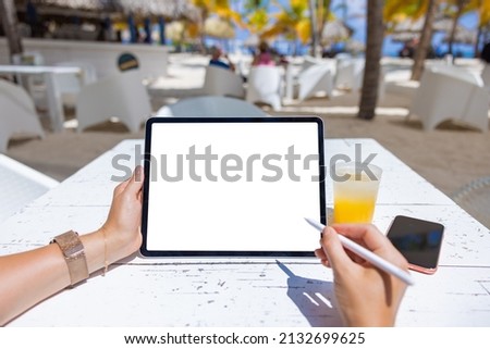Woman using tablet with stylus pen in tropical beach bar, blank white screen mockup