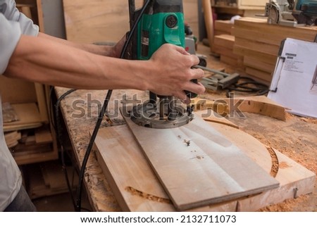 Cutting a round shape from a thick slab of wood. Using a plunge wood router with a circle cutting jig. Making the head of a bar stool at a workshop. Royalty-Free Stock Photo #2132711073