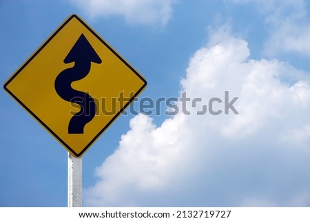 Yellow traffic sign with twisty arrow symbol to warn drivers be careful when driving on twisty way road. Concept : Warning traffic sign for transportation. Blue sky scene.                         