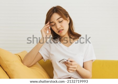 Sick low immunity Asian woman feeling dizzy, sitting on the sofa with flu symptoms, preparing medicine in hand to eat to relieve sickness : Health care for a woman who is sick with a cold and flu.