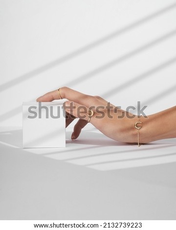 A hand holding a small white box on white background with shadows. Women hand with gold ring