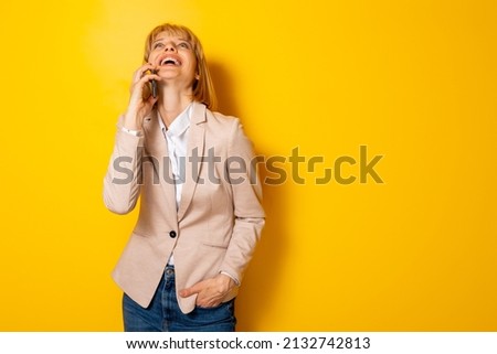 Beautiful woman having a phone conversation and laughing isolated on yellow colored background with copyspace