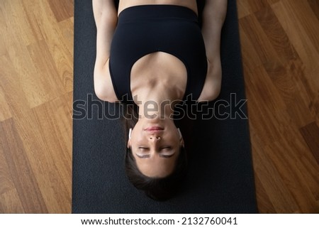 Above view serene beautiful woman in black sport top relax lying on mat in Corpse Savasana pose Dead Body position, listen soothing music through earbuds. No stress, meditation, yoga practice concept Royalty-Free Stock Photo #2132760041