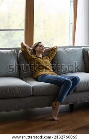 Vertical view serene woman relax on sofa with eyes closed and hands behind head enjoy carefree day off, breath fresh air, climate control inside for comfort living. Tenant, modern smart house concept Royalty-Free Stock Photo #2132760065