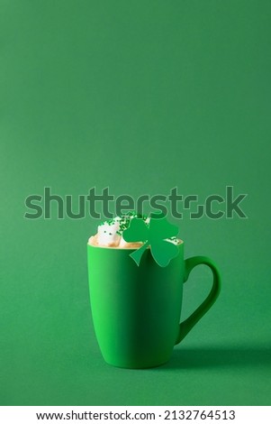 Irish coffee in green cup with whipped cream and sprinkles for St Patricks Day on green background. Close up. Copy space. Vertical format. Minimal style. Monochrome.