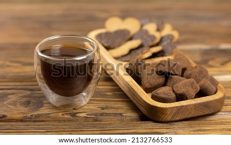 Close-up of chocolate cookies with heart-shaped candies and a cup of coffee on a wooden background. A symbolic image. The concept of a delicious snack. Sweet dessert. Selective focus.